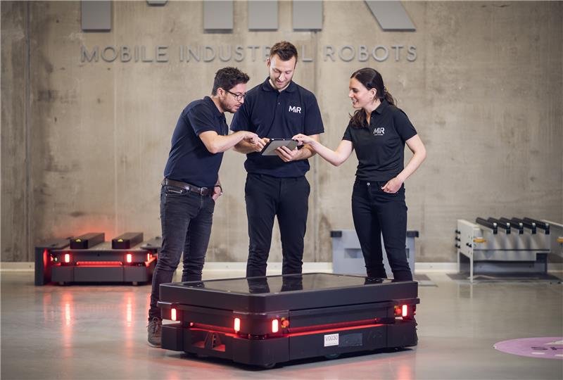 Tecnici MiR in showroom attorno a un robot mobile autonomo con tablet