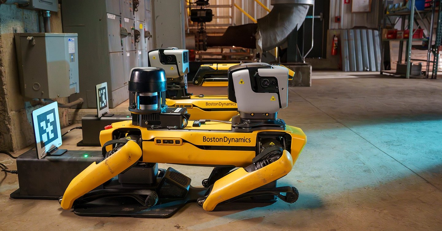 Due robot Spot di Boston Dynamics in stazione di ricarica automatica in ambiente industriale