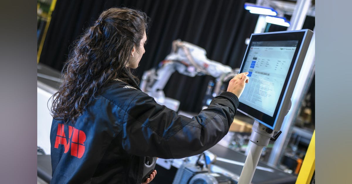 Operatrice programma un robot industriale tramite touchscreen in una cella di produzione