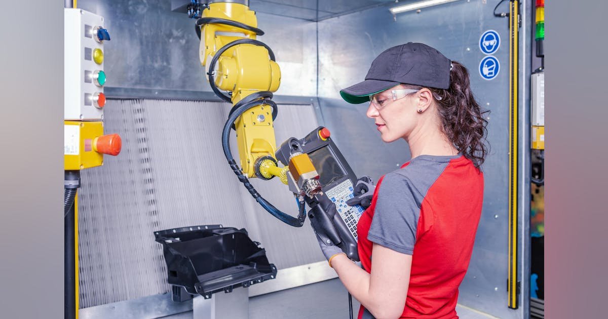 Operatrice con DPI utilizza teach pendant FANUC in una cella robotizzata