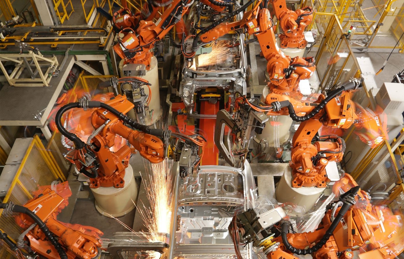 Robot industriali arancioni al lavoro in una linea produttiva automobilistica