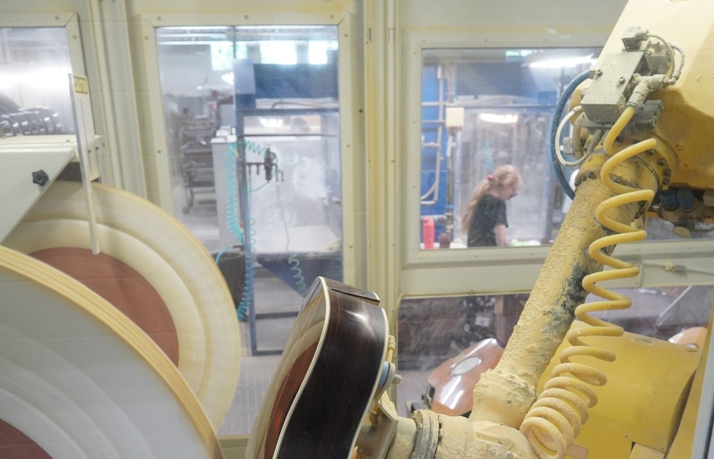 Braccio robotico che lucida una chitarra in una fabbrica con operatore dietro la protezione