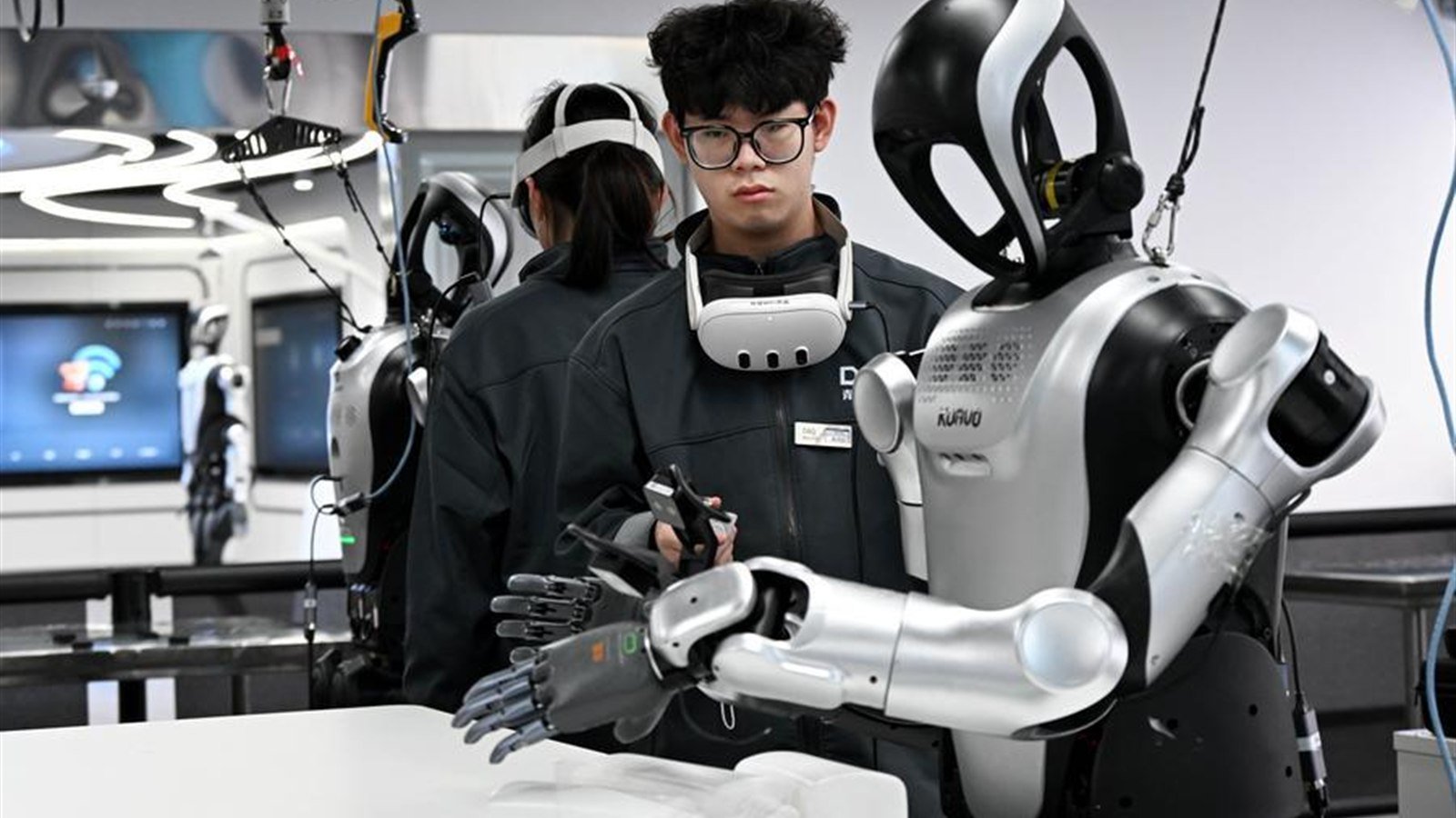 Robot umanoide in laboratorio con oggetti quotidiani e tecnici che osservano da distanza sicura